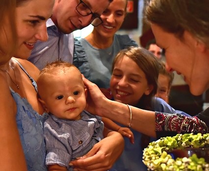 eine Frau hält ein Baby auf dem Arm, eine andere Hand legt sich segnend auf die Wange des Kindes